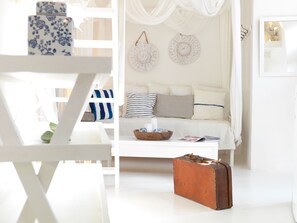A white room with a sofa, a white coffee table, a brown suitcase, and decorative items. - Alsaki Suite Street View by K&K (Oia)