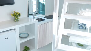 Una cocina moderna con muebles blancos, un lavamanos empotrado y un refrigerador pequeño.