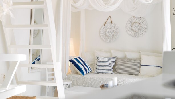 Una habitación blanca con una cama, una escalera y una cesta tejida.