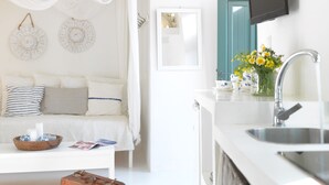 Una habitación moderna y minimalista con una cama blanca, una mesita con objetos decorativos, un televisor montado en la pared y un lavabo con espejo.