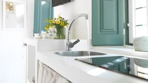 Una cocina con encimera blanca, pileta de acero inoxidable, un jarrón con flores amarillas y puertas color turquesa.