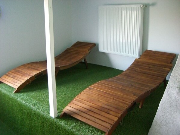 A room with two wooden loungers on artificial grass, a white radiator, and a white pillar.