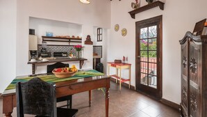 Un'area pranzo con tavolo e sedie in legno, una cucina sullo sfondo e vista all'esterno tramite un'ampia finestra.