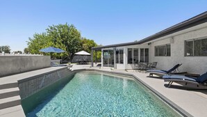 Piscina com água cristalina, rodeada por um deck de concreto e um espaço coberto com área de estar ao ar livre.
