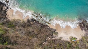 Eine Vogelperspektive eines Strandes mit klarem, türkisblauem Wasser, sandigem Ufer und felsigen Klippen.