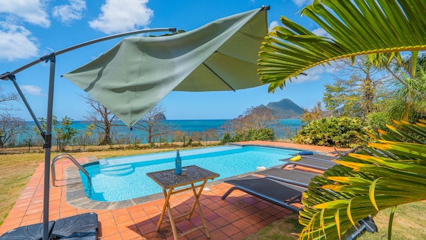 Ein Poolbereich mit Blick auf das Meer und die Berge, einem Tisch und Liegestühlen.