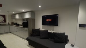 Un salon moderne avec un canapĂ© gris foncĂ©, une petite table dâappoint blanche et un tĂ©lĂ©viseur Ă Ă©cran plat affichant le logo « NETFLIX ».