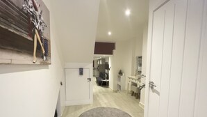 Un couloir avec un tapis rond, une porte blanche, un petit bureau et un miroir.