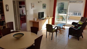 Un salon comprenant une table à manger, des chaises, un téléviseur et un balcon aménagé avec du mobilier d’extérieur.