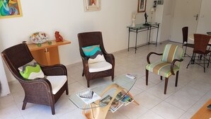 Un salon avec des fauteuils en osier, une table basse en verre et une petite table d’appoint agrémentée d’objets décoratifs.