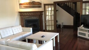 Een woonkamer met een witte leren bank, een open haard, een televisie en een trap.
