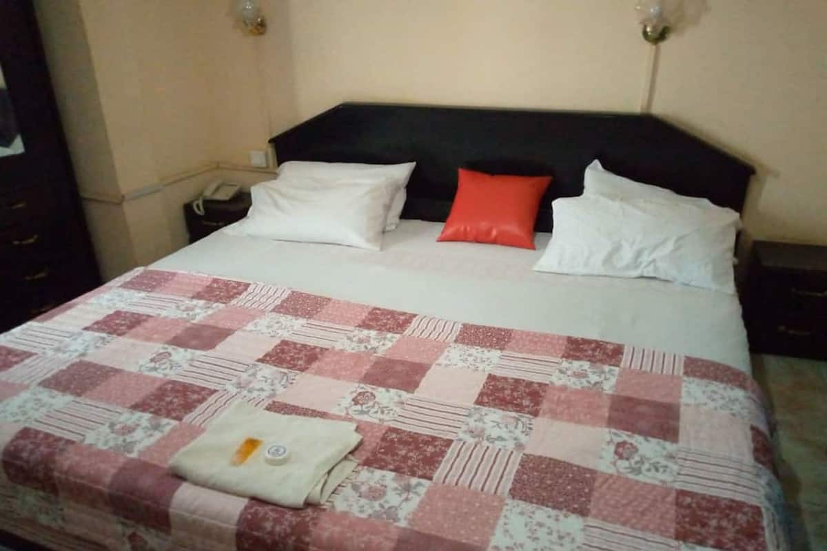 A bed with a checkered quilt, a red pillow, and a folded towel on it.