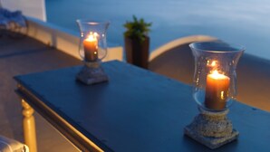 Deux bougies allumées, placées dans des photophores en verre, sur une table près d’une fenêtre donnant sur la mer.