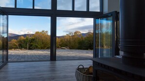 A room with a large glass door leading to an outdoor area with a stone patio and a view of mountains and trees. - Relax and Refuel to the Rhythm of Nature at Fia Lodge. (Glencar)