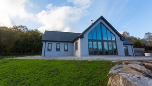A modern house with a large glass facade, a sloped roof, and a stone pathway leading to the entrance. - Relax and Refuel to the Rhythm of Nature at Fia Lodge. (Glencar)