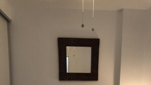 A neatly made bed with white linens and two pillows, a bedside table with a lamp, and a wall-mounted mirror with a decorative frame. - Francisco Cano bowling (Fuengirola)