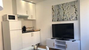 A modern kitchen with white cabinets, a microwave, and a coffee maker. A flat-screen TV is mounted on a white console below a wall-mounted artwork. - Francisco Cano bowling (Fuengirola)