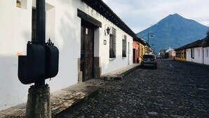 Una calle empedrada flanqueada por edificios tradicionales, con una montaña al fondo y un coche estacionado.