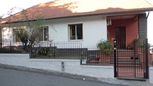 Una casa de un piso con tejado de tejas rojas, fachada blanca y cerca de metal negro.