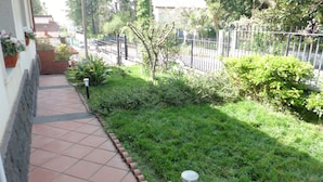 Un camino conduce a un edificio con acceso de baldosas y un pequeño jardín con césped y plantas.
