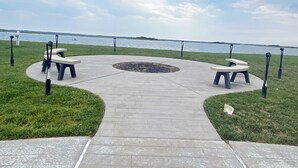 Un parc doté de tables de pique-nique et de bancs disposés en demi-cercle autour d’un foyer central, avec vue sur une étendue d’eau.