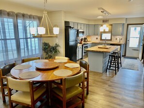 A modern kitchen with a central island, wooden dining table with chairs, and a hanging light fixture. - 3 BR House, 2 Blocks To Beach, Nice Backyard For Grilling (Wildwood Crest)