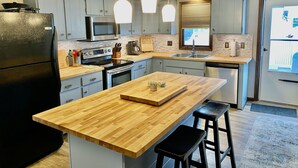 Une cuisine moderne avec des meubles gris, un réfrigérateur noir, un îlot central en bois et des luminaires suspendus.