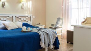 A neatly made bed with a blue bedspread, a white headboard, and a tray with a teapot and cups. There are two wall-mounted lamps, a small table with a lamp, and a chair with a towel draped over it. - Appartement au calme 8p, près de la plage (Pornichet)
