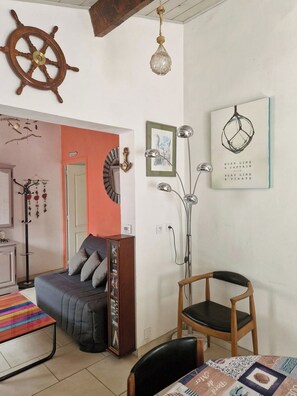 A living room with a sofa, a chair, a table, a ship's wheel, a hanging light, and wall art.