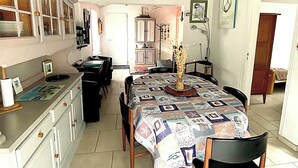 Une cuisine compacte avec un coin repas, agrémentée d’une décoration en forme de roue de navire, d’une table recouverte d’une nappe à motifs et d’un vase rempli de fleurs.