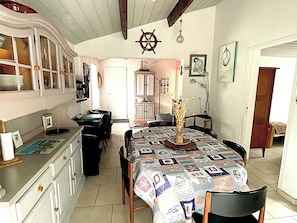 A compact kitchen with a dining area, featuring a ship's wheel decoration, a table with a patterned tablecloth, and a vase with flowers.