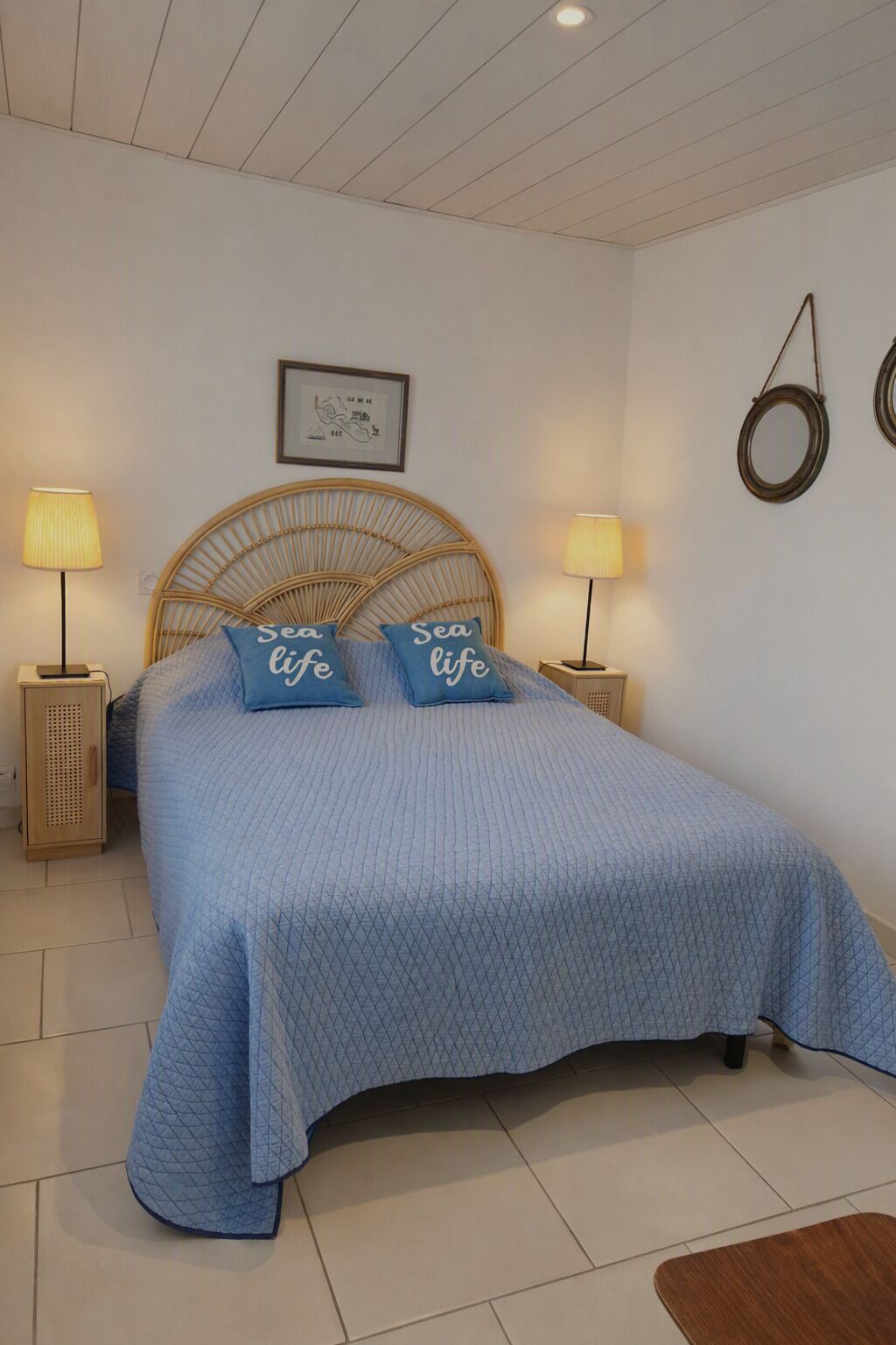 Een slaapkamer met een bed, twee bedlampen, een lijst met een afbeelding aan de muur en een ronde decoratie aan de wand.