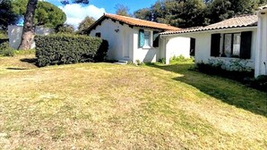 Un bâtiment blanc avec un toit en tuiles, une cour verdoyante et un grand arbre.