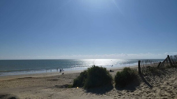 Une plage ensoleillée, un ciel dégagé et quelques personnes se promenant sur le sable.