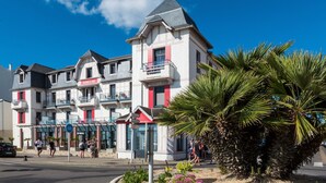 A multi-story hotel with balconies, a bike parking sign, and a palm tree in the foreground. - Studio cosy et équipé, près de la plage (Pornichet)