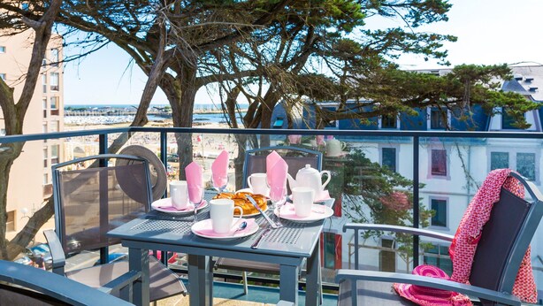 A balcony with a table set for breakfast, overlooking a beach and buildings. - Studio cosy et équipé, près de la plage (Pornichet)