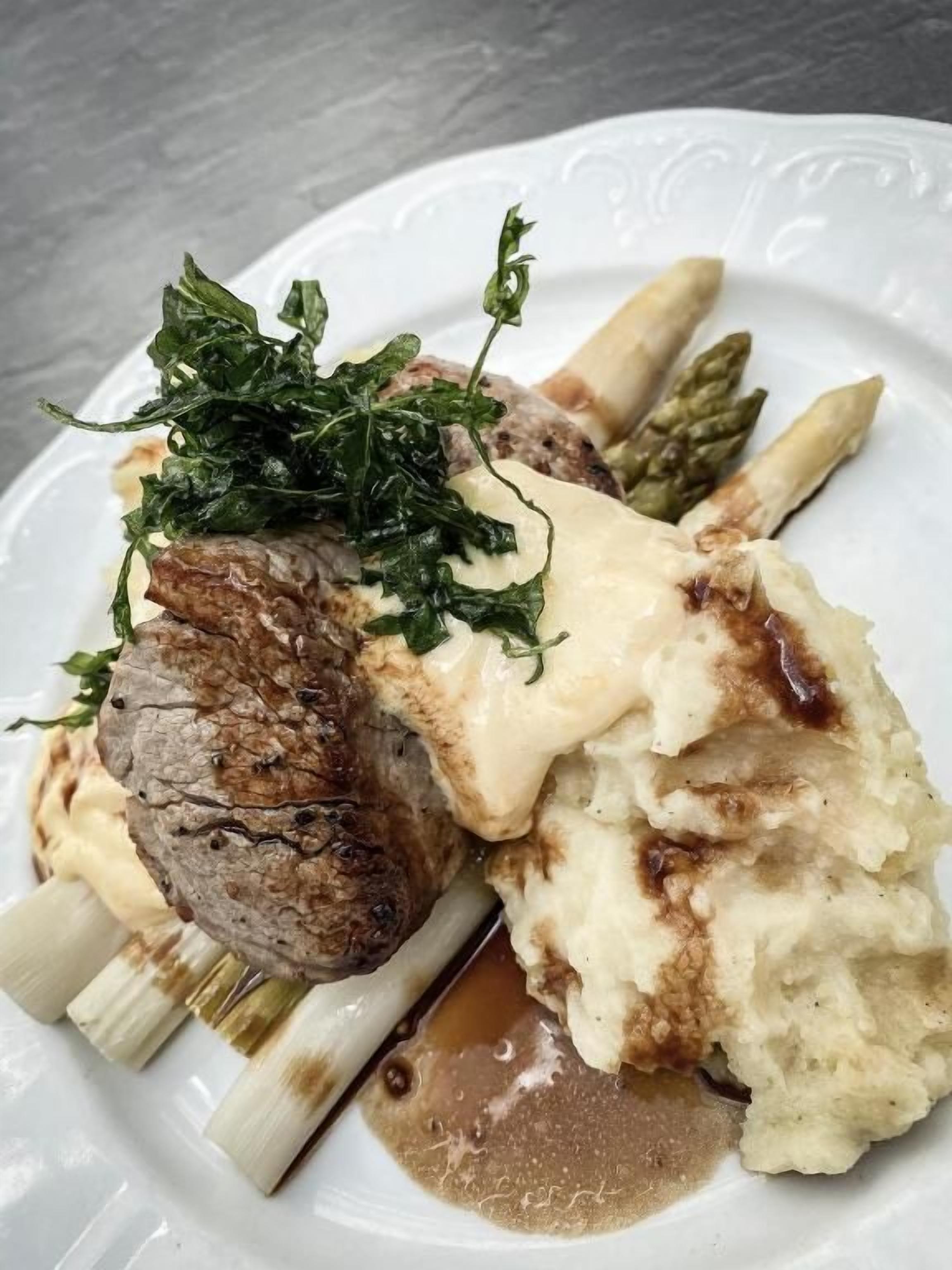 A plate with a steak, mashed potatoes, asparagus, and a garnish.
