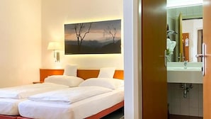 Habitación de hotel con dos camas, un cuadro en la pared, baño visible a través de una puerta abierta y una alfombra estampada.