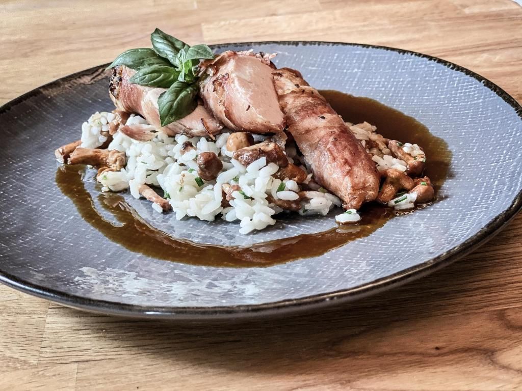 A plate with a dish consisting of rice, mushrooms, and a piece of meat, possibly pork, garnished with a basil leaf.
