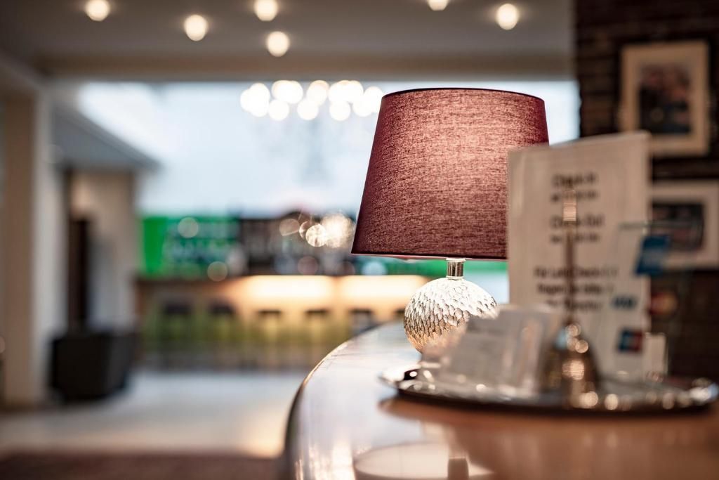 A lamp with a textured shade on a reflective surface, possibly a table, with a blurred background suggesting a public space.