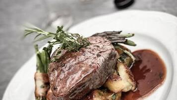 A plate with a steak, potatoes, and a sauce, accompanied by a glass of wine and a bottle of liquor.