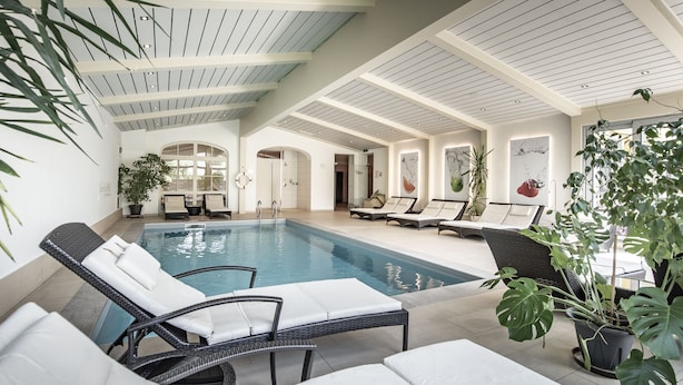 Una piscina interior con sillones de descanso y plantas en macetas.