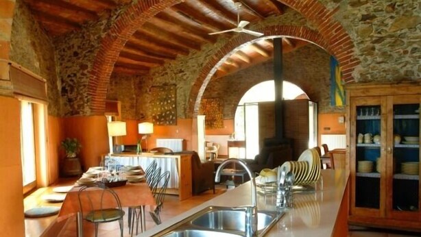A rustic kitchen with stone walls, a wooden ceiling, and a central island with a sink. - Rural house (full rental) Mas Hortus for 13 peopleOffers (Garriguella)