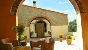 An outdoor seating area with wicker furniture and potted plants, leading to a building with a stone facade and a wooden door. - Rural house (full rental) Mas Hortus for 13 peopleOffers (Garriguella)