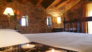 A rustic stone-walled room with a bed, two wall-mounted lamps, and a candle on a tray. - Rural house (full rental) Mas Hortus for 13 peopleOffers (Garriguella)