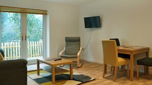 Un salon moderne avec un canapé, une table, un téléviseur fixé au mur et une vue sur l’extérieur grâce à une porte-fenêtre coulissante.