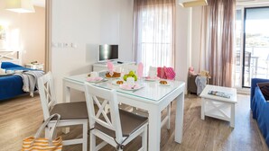 Una habitación de hotel moderna con comedor, televisión y balcón con cortinas.