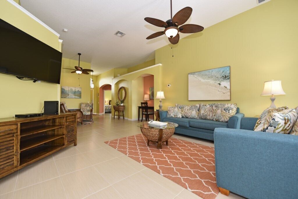A living room with a blue sofa, a wooden entertainment unit, and a ceiling fan.