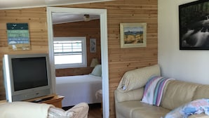 A cozy room with a wooden floor, a beige sofa, a television, and a bed. - River Meadow Camp Cottage (Summerside)