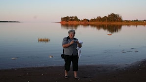 A person standing on a beach near calm water with a distant tree line. - River Meadow Camp Cottage (Summerside)